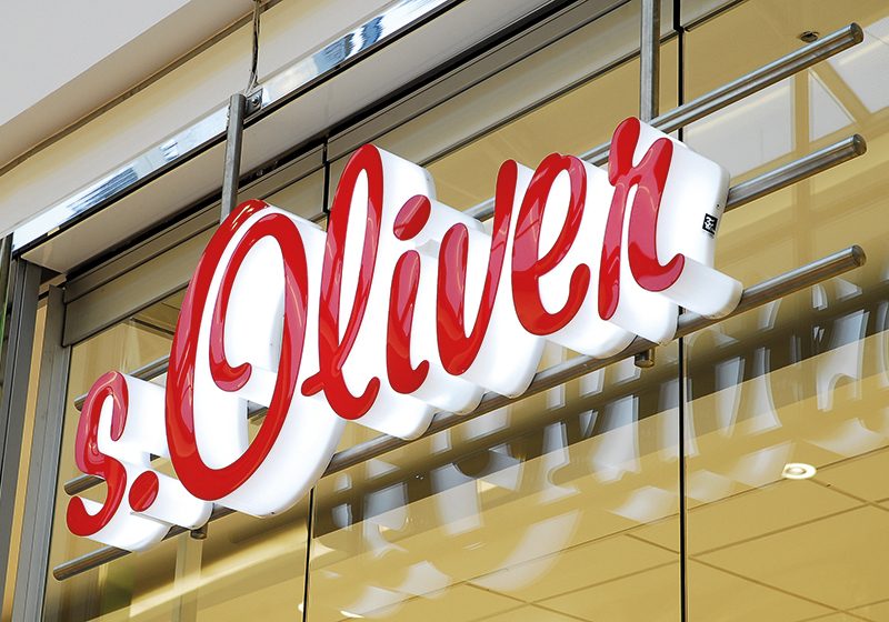 Rote Einzelbuchstaben des Schriftzugs s.Oliver, montiert auf Edelstahlrohren vor einer Glasfassade