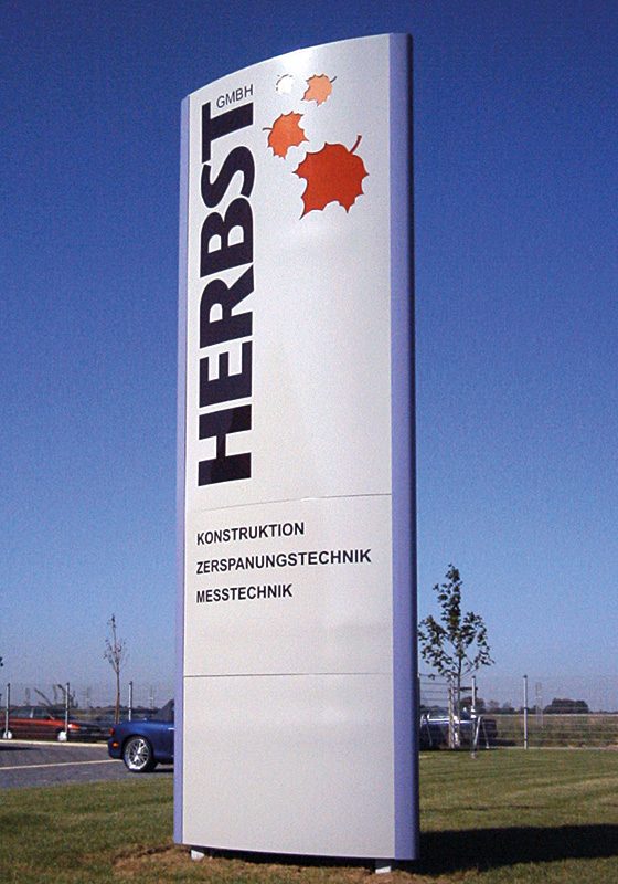 Freistehender, leicht gebogener Pylon der Herbst GmbH mit ausgeschnittenen, beleuchteten Herbstblättern